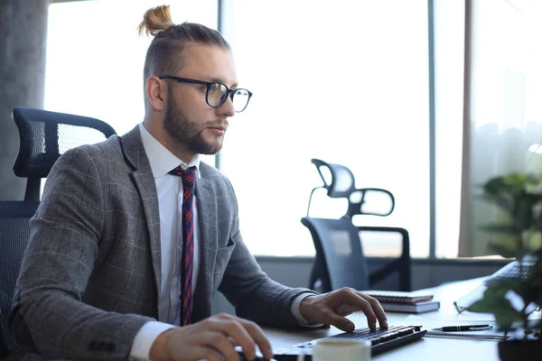 Задуманный молодой человек в полном костюме, работающий за компьютером, сидя в офисе . — стоковое фото