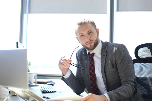 Gut aussehender junger Mann, der im Büro mit der Brille in der Hand in die Kamera blickt. — Stockfoto