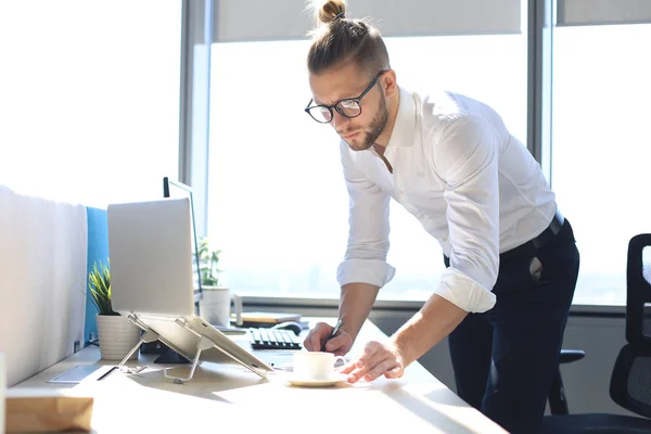 Joven reflexivo escribiendo algo mientras trabaja en el espacio de trabajo creativo . — Foto de Stock