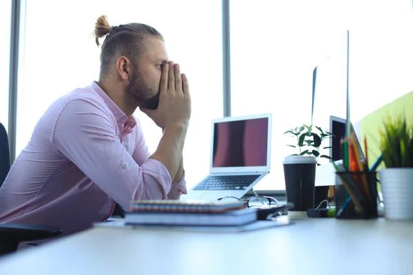 Short of tired young man in smart casual wear keeping face in hands while sitting in the office. — Stock Photo, Image