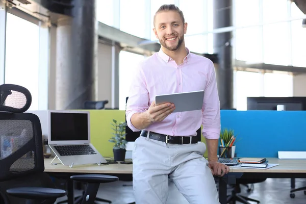 Jovem empresário moderno que trabalha usando tablet digital enquanto está sentado no escritório . — Fotografia de Stock