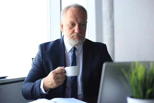 Reifer Geschäftsmann arbeitet am Computer und trinkt Kaffee im modernen Büro. — Stockfoto