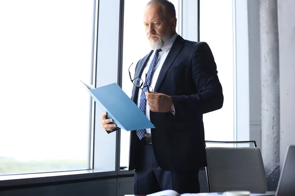 Σοβαρός ώριμος επιχείρηση άνθρωπος σε τυπογραφεί σύμβαση ανάγνωσης ενώ στέκεται κοντά στο παράθυρο στο γραφείο. — Φωτογραφία Αρχείου