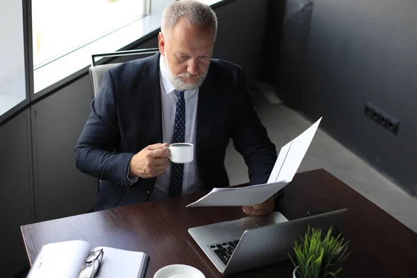 Allvarliga mogna affärsman i Formalwear läsning kontrakt när du sitter vid skrivbordet på kontoret. — Stockfoto