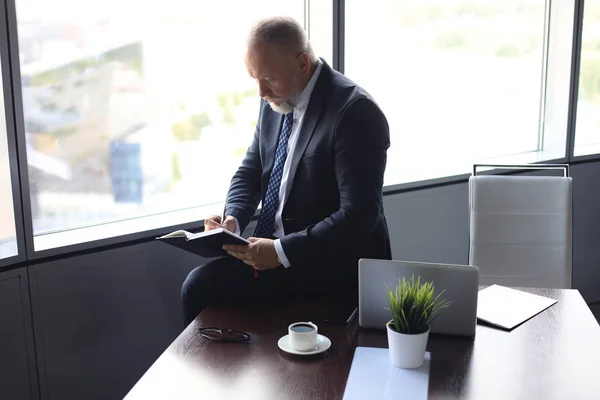 Фокусований зрілий бізнесмен працює і робить нотатки в своєму сучасному офісі . — стокове фото