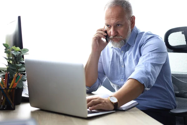 Homme d'affaires mature confiant ayant un appel téléphonique sur son smartphone dans un bureau moderne . — Photo