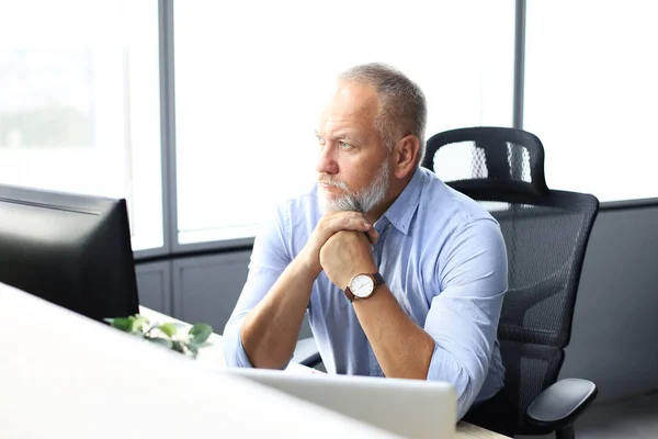 Fokuserad mogen affärsman djupt i tanken när du sitter vid ett bord i moderna kontor. — Stockfoto