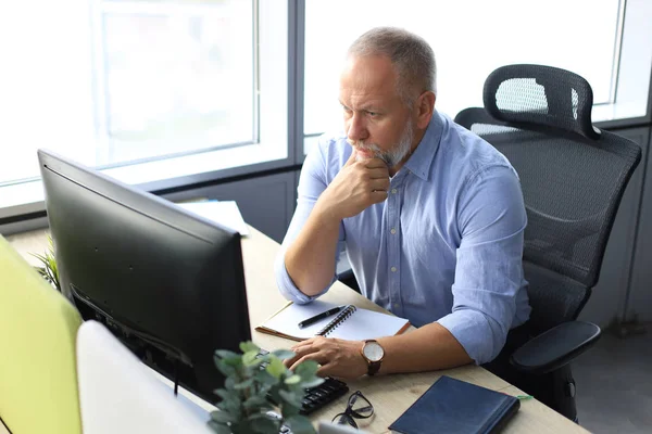 Focalizzato maturo uomo d'affari profondo nel pensiero mentre seduto a un tavolo in ufficio moderno . — Foto Stock