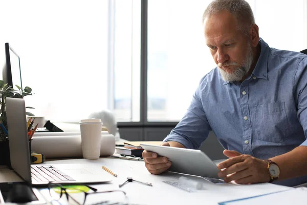 Зрелый бизнесмен, работающий с цифровым планшетом, сидя в современном офисе . — стоковое фото