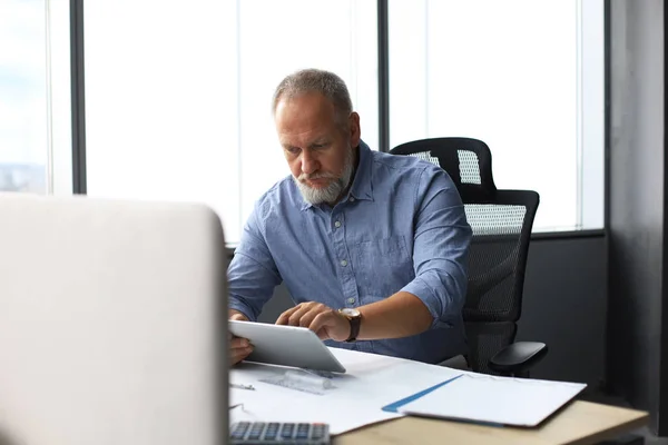 Зрелый бизнесмен, работающий с цифровым планшетом, сидя в современном офисе . — стоковое фото