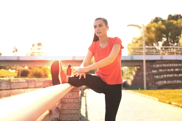 Aantrekkelijke jonge fitnessvrouw die sportkleding draagt, buiten traint, oefeningen uitrekt. — Stockfoto