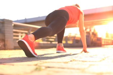 Açık havada koşarken başlangıç çizgisinde duran spor giyim genç kadının üst arka görünümü.