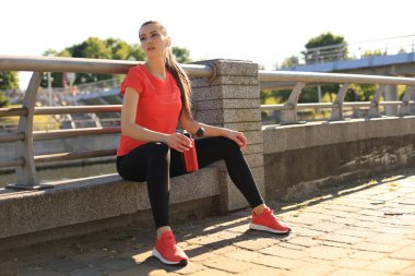 Spor giyim çekici genç kadın açık havada otururken bir mola.