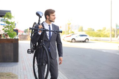 Açık havada yürürken bisikletini omuzda taşıyan yakışıklı genç işadamı.