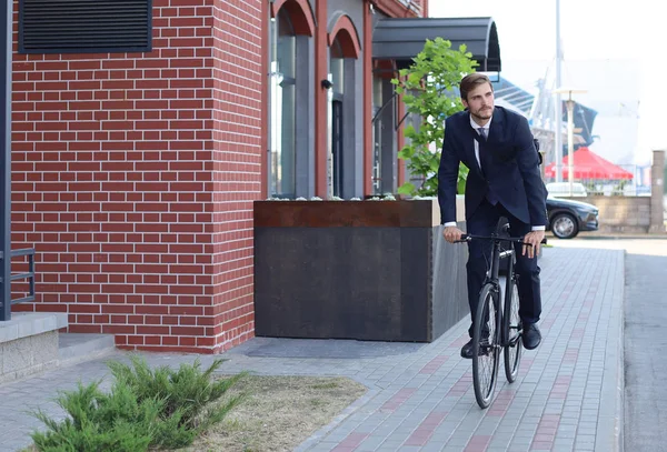 Jovem homem de negócios elegante vestido de terno andando de bicicleta em uma rua da cidade . — Fotografia de Stock