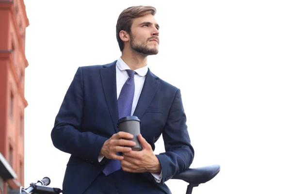 Ένας νέος επιχειρηματίας που κρατά φλιτζάνι καφέ ενώ στέκεται με το ποδήλατό του κοντά στο κτίριο του γραφείου στο παρασκήνιο. — Φωτογραφία Αρχείου