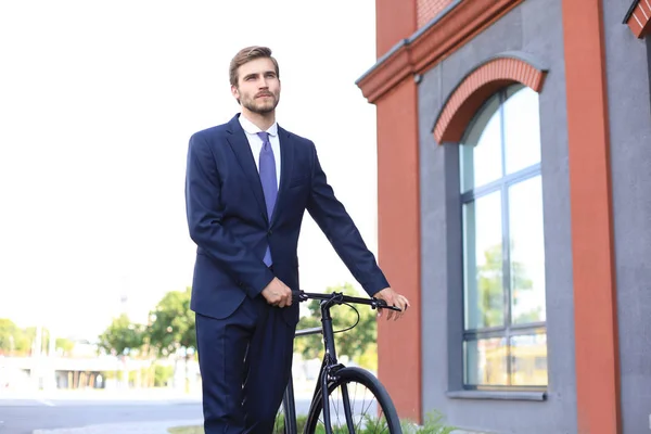 Young stylish business man dressed in suit walking with a bicycle on a city street.