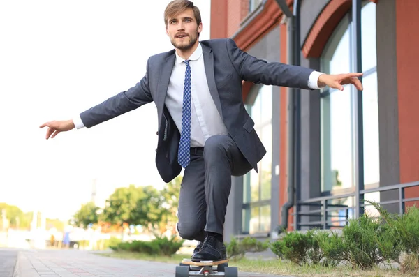 Jeune homme d'affaires confiant en costume d'affaires sur longboard se précipitant à son bureau, dans la rue dans la ville . — Photo