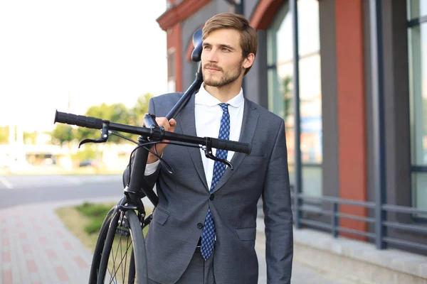 Pohledný mladý obchodník, který při chůzi venku nosí kolo na rameni. — Stock fotografie