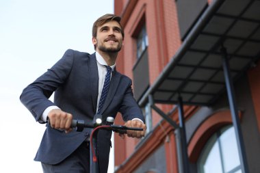 Takım elbiseli genç, iş toplantısında elektrikli scooter'a biniyor. Ekolojik ulaşım kavramı.