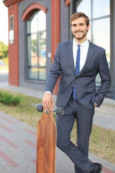 Jovem empresário confiante andando na rua, usando longboard . — Fotografia de Stock