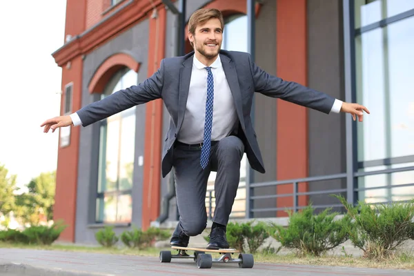 Selbstbewusster junger Geschäftsmann im Businessanzug auf Longboard eilt in sein Büro, auf der Straße in der Stadt. — Stockfoto