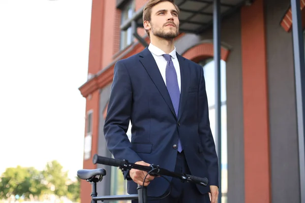 Νέος κομψός επιχειρηματικός άνθρωπος ντυμένος με κοστούμι περπάτημα με ένα ποδήλατο σε ένα δρόμο της πόλης. — Φωτογραφία Αρχείου