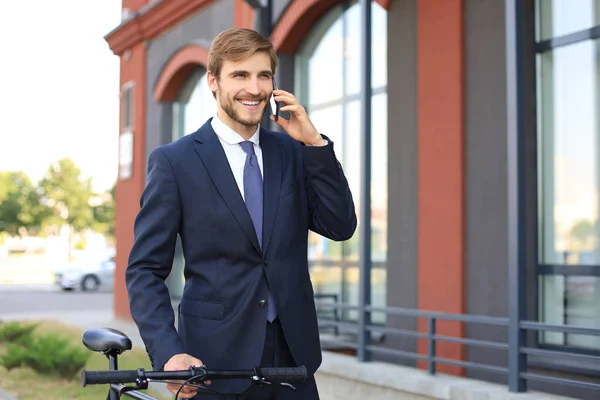屋外で自転車で立ちながら、スーツに身を包んだ笑顔の若いビジネスマンの肖像画. — ストック写真