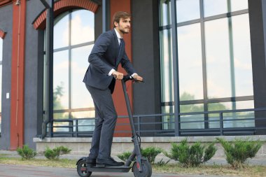 Şehir caddesinde elektrikli scooter kullanan genç iş adamı. Modern ve ekolojik ulaşım konsepti.