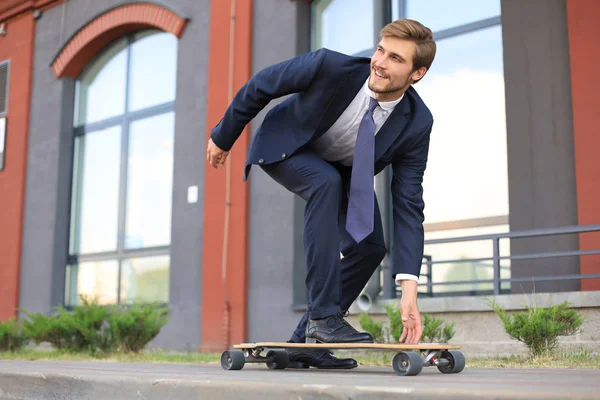Selbstbewusster junger Geschäftsmann im Businessanzug auf Longboard eilt in sein Büro, auf der Straße in der Stadt. — Stockfoto