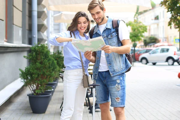 Hermosa pareja joven sosteniendo un mapa y sonriendo mientras está al aire libre. —  Fotos de Stock