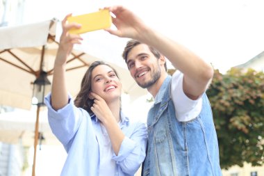 Yaz lık güzel genç çift, şehir caddesinde yürürken birlikte gülümseyip selfie çekerken.