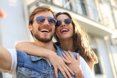Açık havada mutlu gülümseyen neşeli genç çift in görüntü kamera ile selfie çekmek.