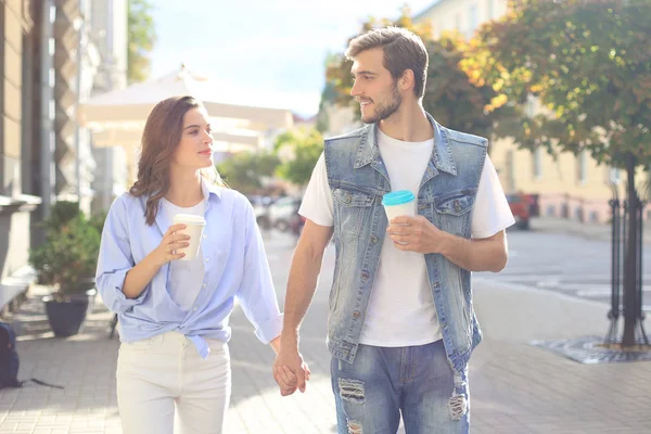 Kép a fiatal pár férfi és nő alkalmi ruhákat ivott elvisz kávét, miközben sétálnak át a város utcai. — Stock Fotó