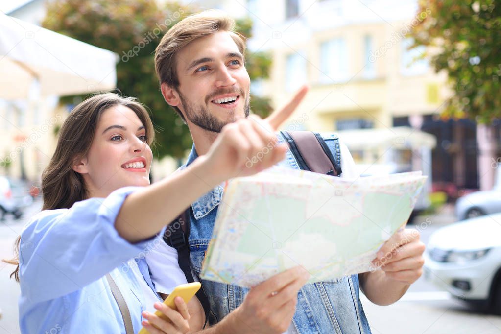 Beautiful young couple holding a map and smiling while standing outdoors.