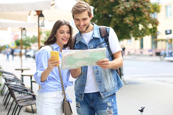 Beau jeune couple tenant une carte et souriant tout en se tenant à l'extérieur. — Photo