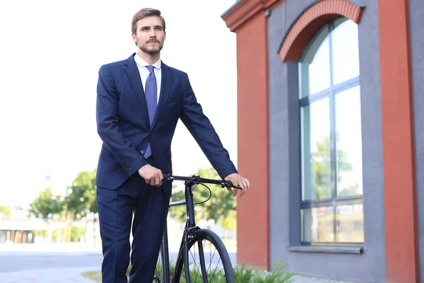 Ung snygg affärsman klädd i kostym Walking med en cykel på en stadsgata. — Stockfoto