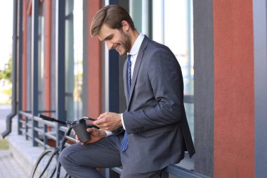 Gülümseyen genç şık adam açık havada bisiklet ile kahve yudumlarken istimal hareket eden telefon.