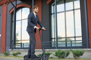 Şehir caddesinde elektrikli scooter kullanan genç iş adamı. Modern ve ekolojik ulaşım konsepti.