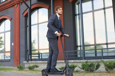 Şehir caddesinde elektrikli scooter kullanan genç iş adamı. Modern ve ekolojik ulaşım konsepti.