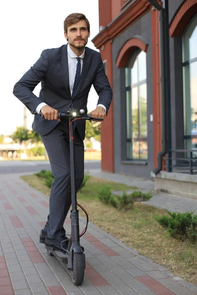 Jeune homme d'affaires en costume roulant sur scooter électrique lors d'une réunion d'affaires. Concept de transport écologique . — Photo