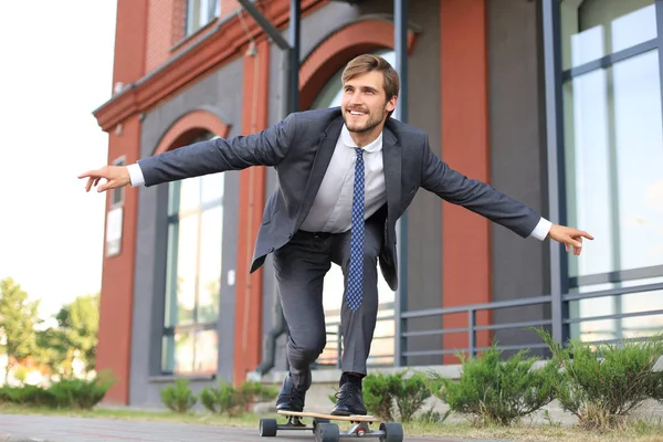 Joven empresario confiado en traje de negocios en longboard apresurándose a su oficina, en la calle de la ciudad . —  Fotos de Stock