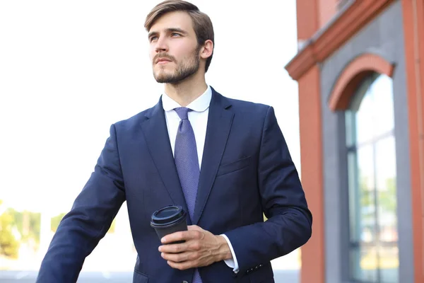 オフィスビルの近くに自転車を持ちながらコーヒーを飲みながら、若いビジネスマンを背景に. — ストック写真