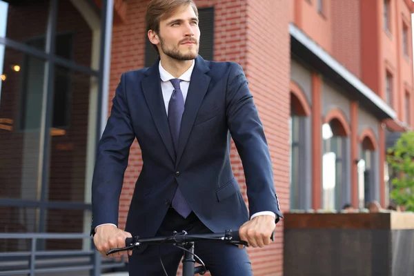 Ung snygg affärsman klädd i kostym rida på en cykel på en stadsgata. — Stockfoto