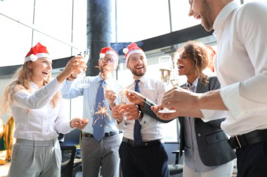 Genç iş ortakları Bengal ışıkları yakıp modern bir ofiste şampanya içiyorlar. Mutlu Noeller ve mutlu yıllar..