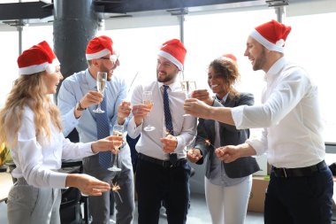Genç iş ortakları Bengal ışıkları yakıp modern bir ofiste şampanya içiyorlar. Mutlu Noeller ve mutlu yıllar..