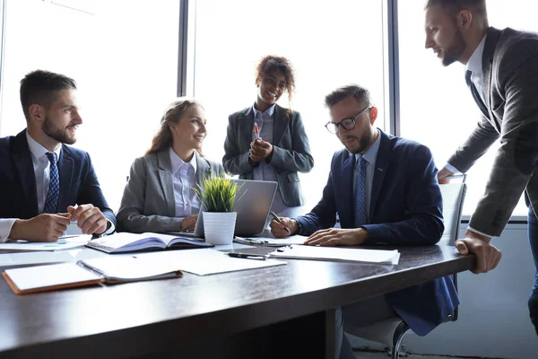 Gruppo di uomini d'affari moderni in abiti formali che discutono di affari e sorridono seduti in ufficio — Foto Stock