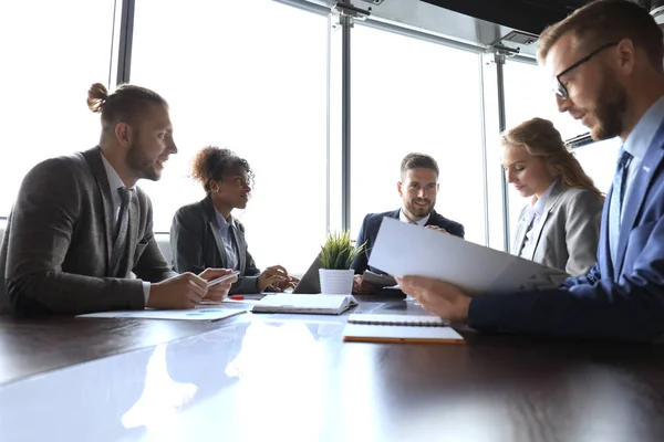 Група сучасних бізнесменів у формальному одязі обговорює бізнес та посміхається сидячи в офісі — стокове фото