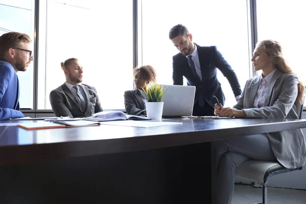 Gruppo di uomini d'affari moderni in abiti formali che discutono di affari e sorridono seduti in ufficio — Foto Stock