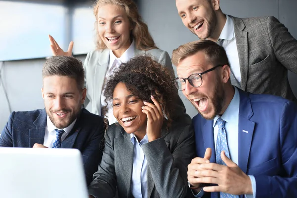 Gli uomini d'affari felici ridono vicino al computer portatile in ufficio. Scherzo di successo dei colleghi di squadra e divertirsi insieme al lavoro. — Foto Stock